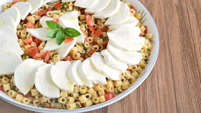 White dish of pasta salad with tomatoes and slices of fresh mozzarella.