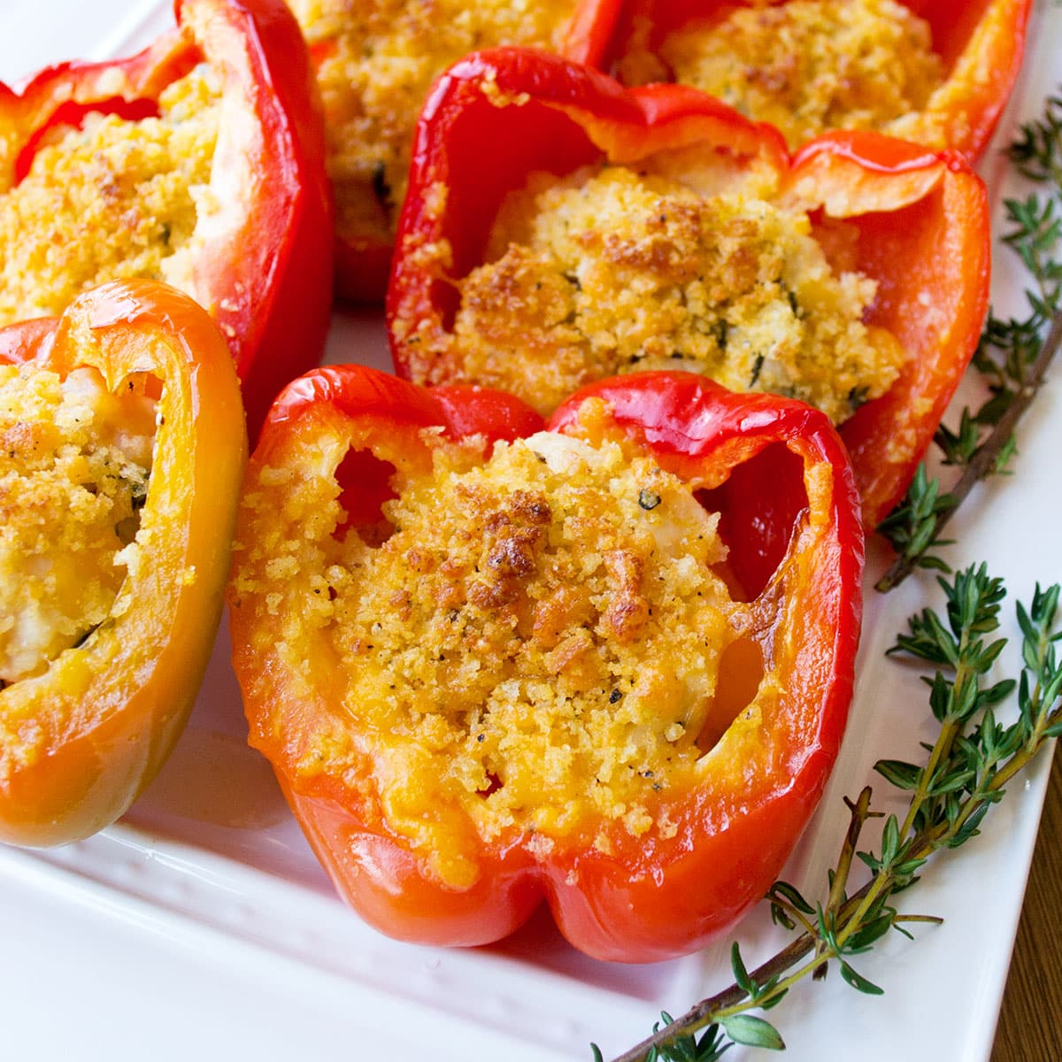Red bell pepper halves stuffed with chicken and cheese and topped with panko breadcrumbs that are browned.