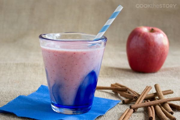 cranberry smoothie in glass with straw and cinnamon sticks to the side.