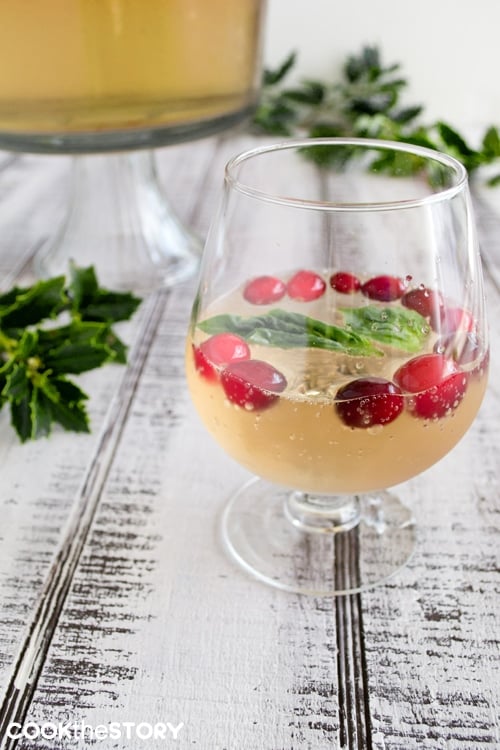 Champagne punch with cranberries and basil leaves in a wide stemmed glass.