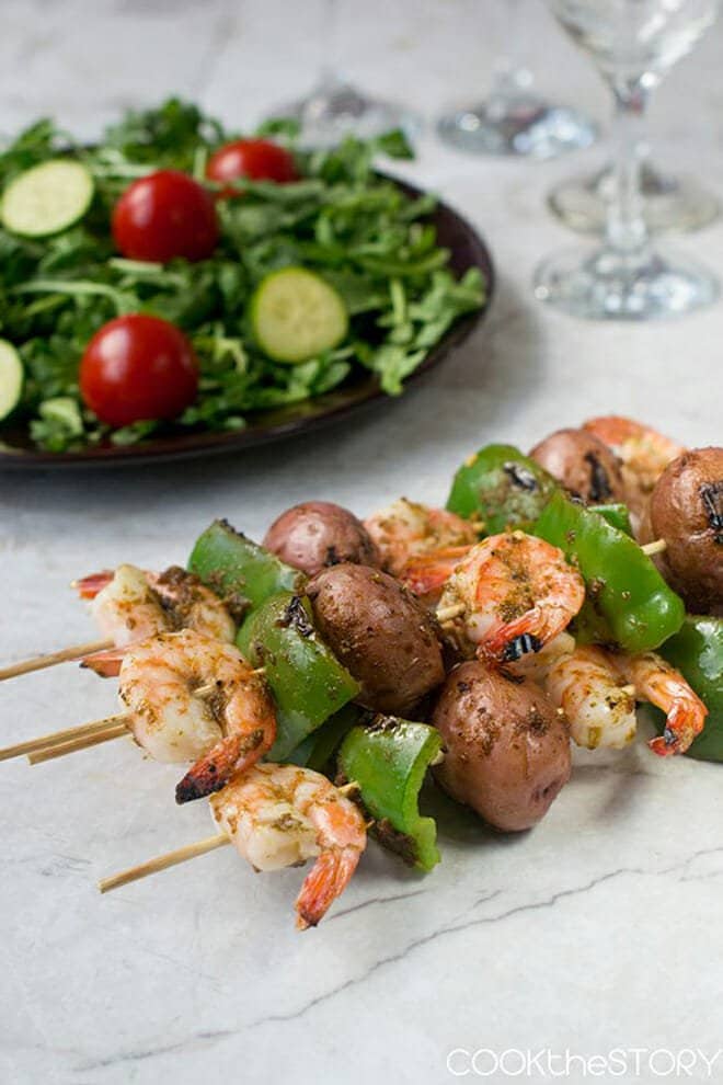 Shrimp, green bell pepper, and potato on wooden skewers, salad in background.