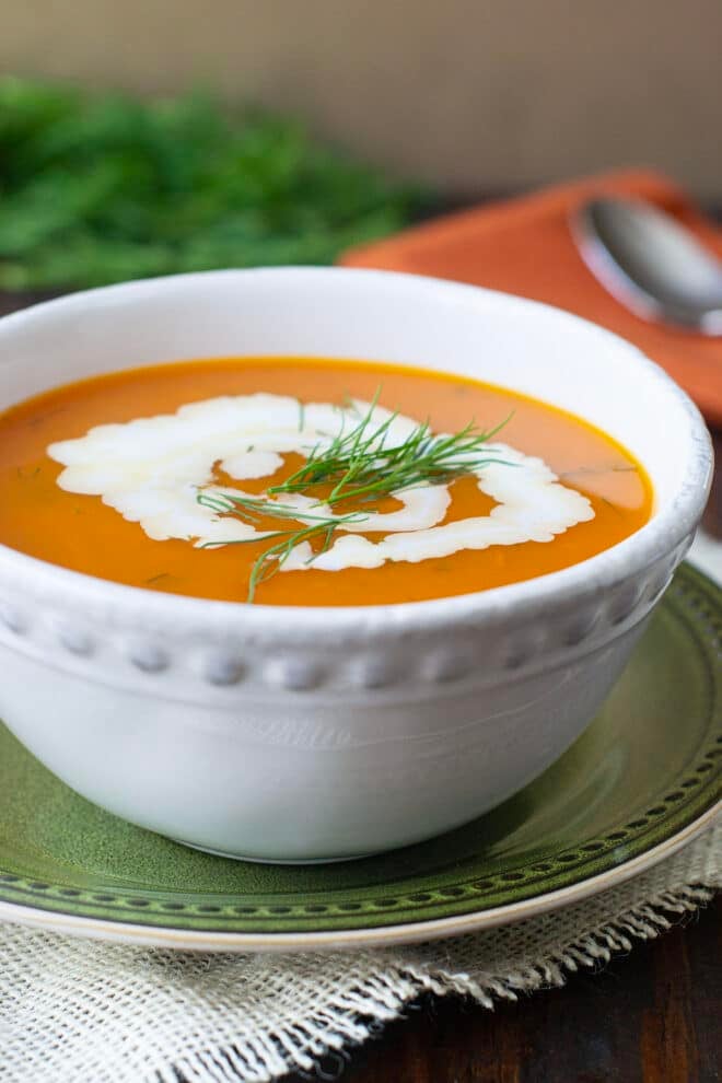 Carrot Soup with cream and fresh dill in a white bowl on a green plate.