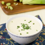 White bowl of potato leek soup with chives on top.