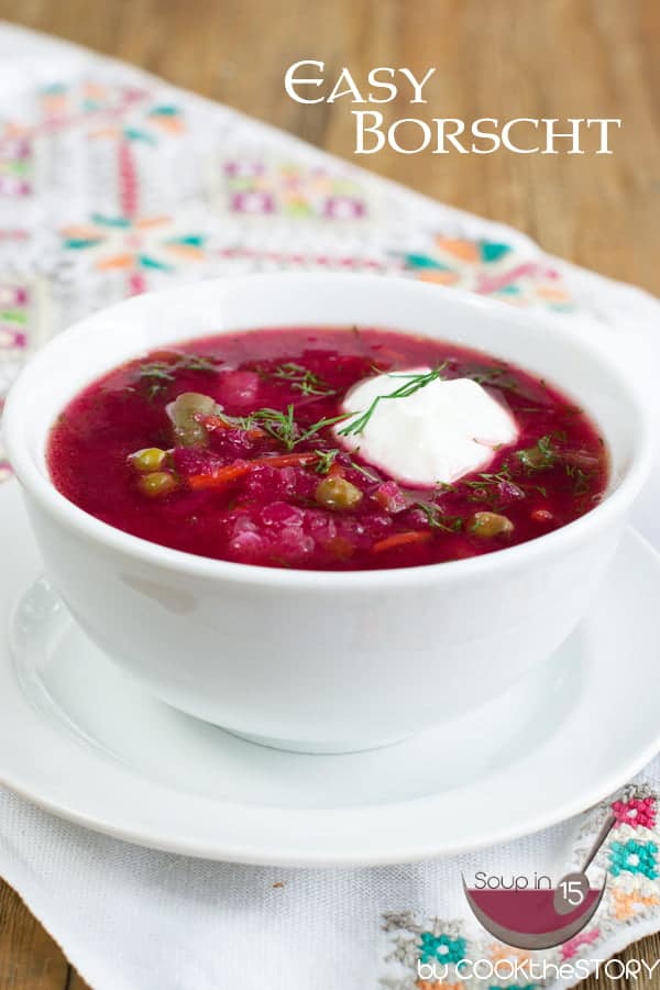 White bowl filled with ruby-red Borscht soup with a dollop of sour cream on top and garnished with chopped dill.