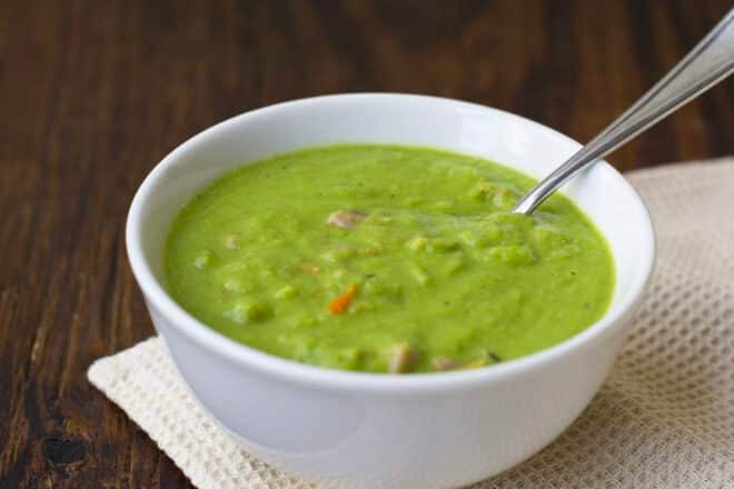 A bowl full of green pea soup dotted with bits of carrot and ham
