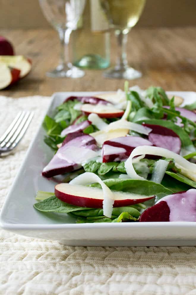 Salad with beets, apples, and shreds of white cheese on a white rectangular platter.