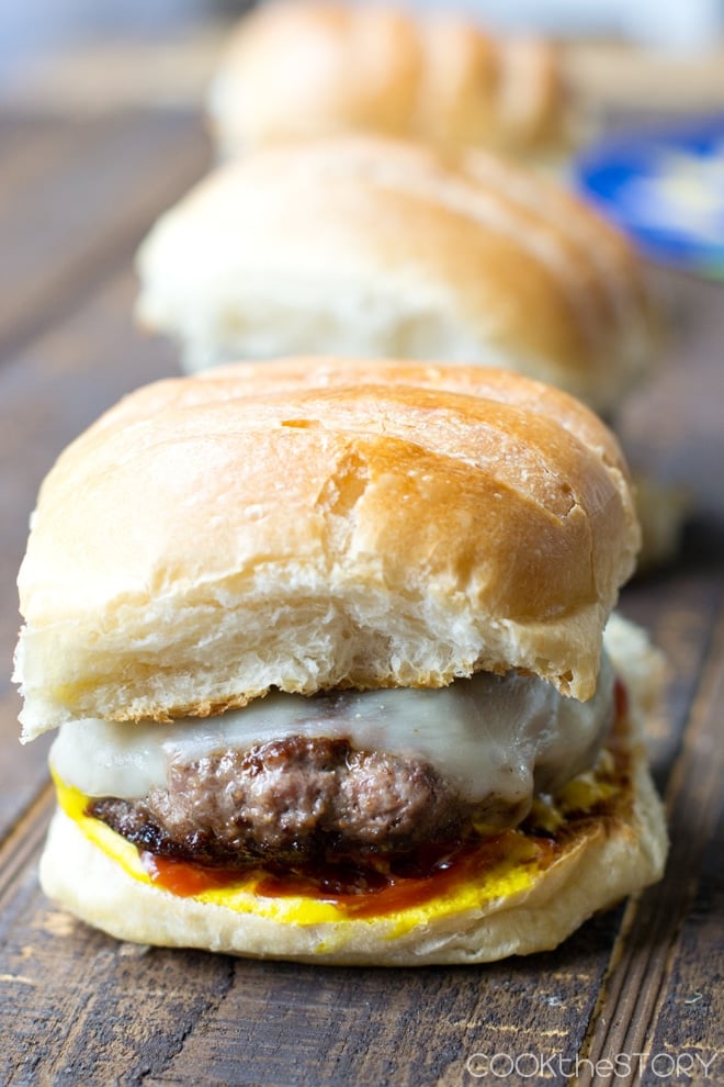 Burgers with buns with cheese, ketchup, and mustard.