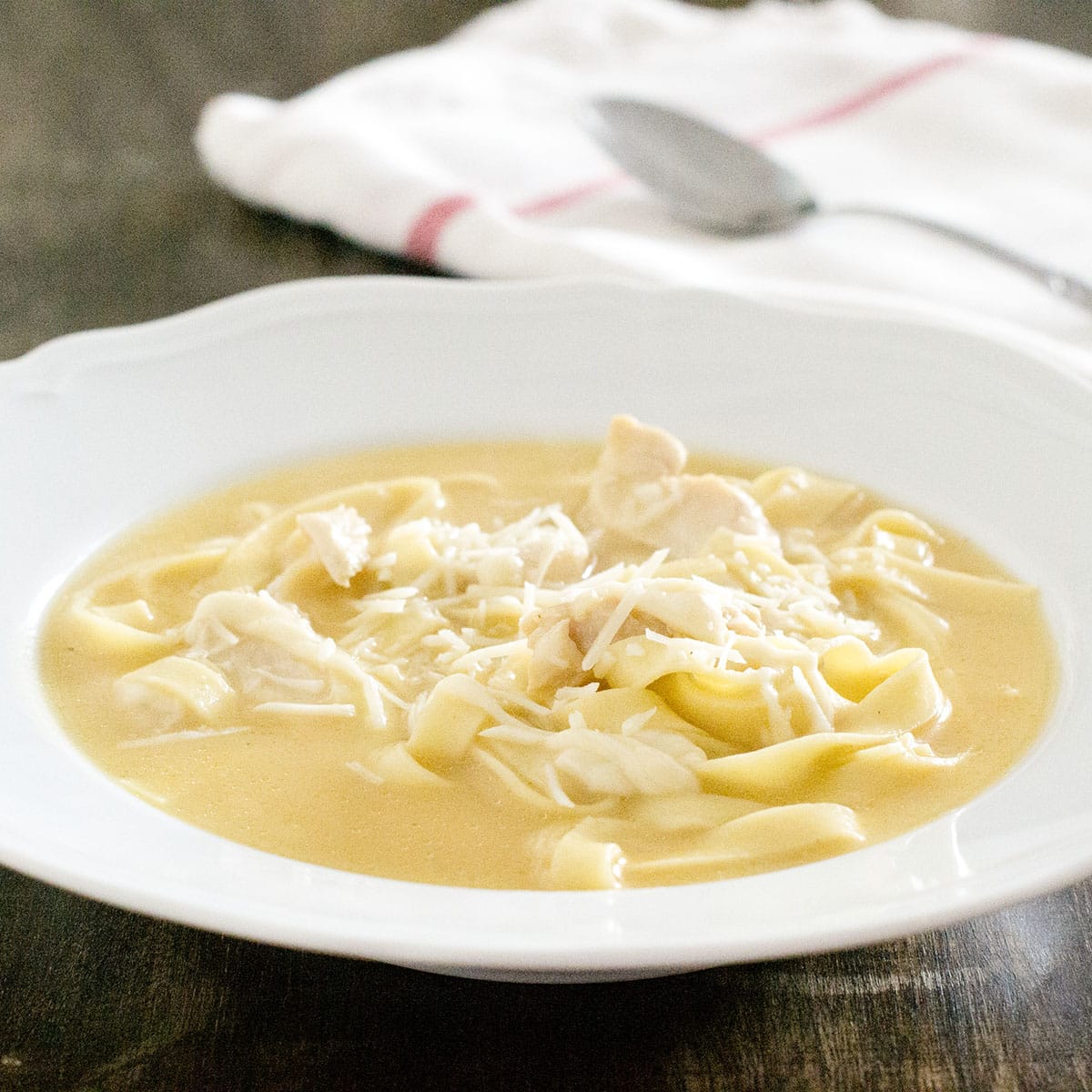 White bowl with chicken fettuccine alfredo soup, topped with grated Parmesan.