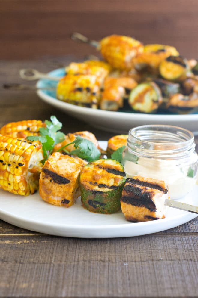 Skewers with chunks of salmon, large slices of zucchini, and pieces of corn on the cob