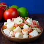 Hearts of palm salad in a wooden bowl, fresh tomato and lime in background.