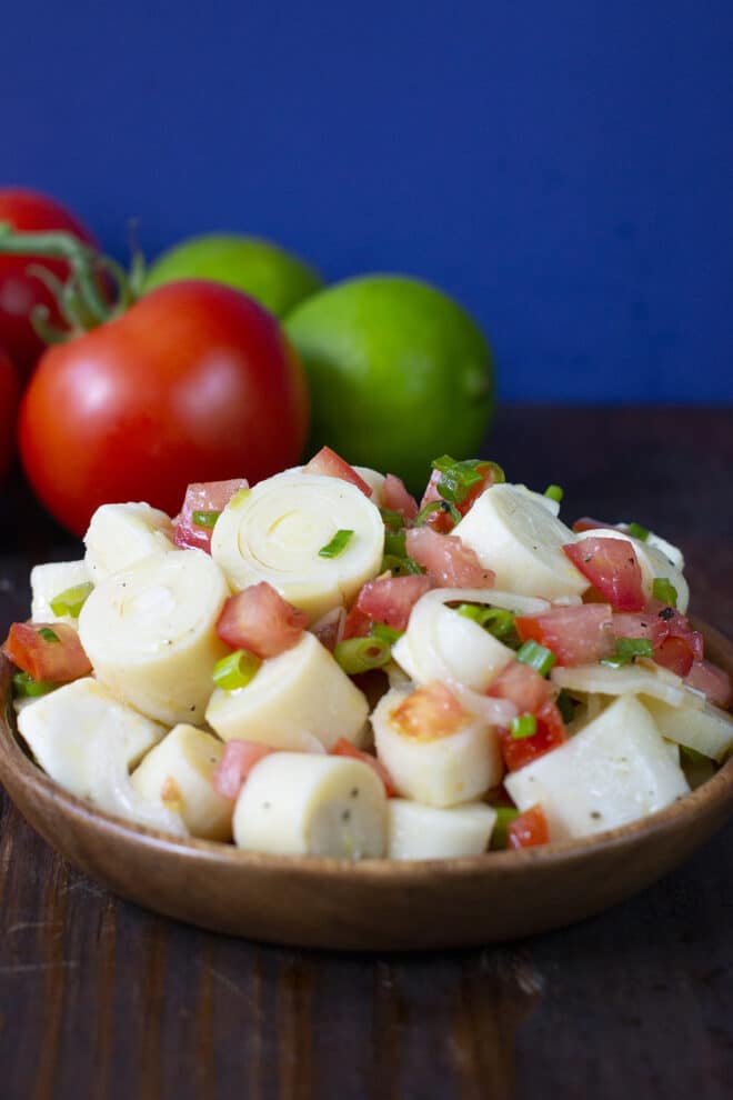 Hearts of palm salad in a wooden bowl, fresh tomato and lime in background.