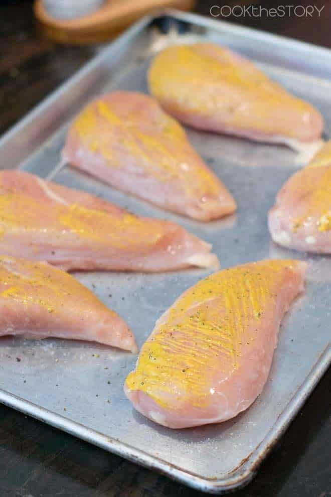 Raw Chicken Breasts on sheet pan with mustard brushed on.