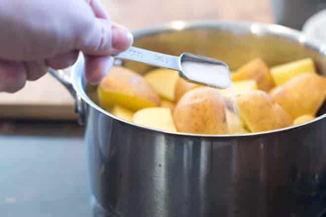 Potatoes in stainless steel pot with salt being added.