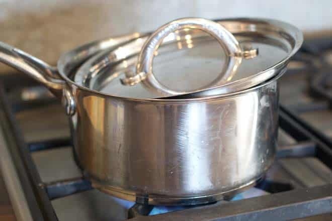 Stainless steel pot on stove with lid partially covering it.