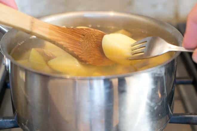 Testing potato over pot with wooden spoon and fork.