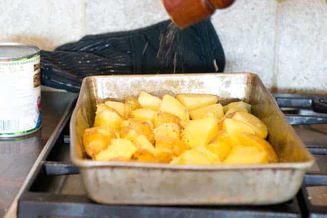 seasoning potatoes in baking pan with pepper
