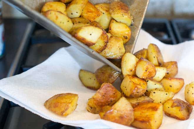 Roasted potatoes being turned out onto paper towel lined plate.