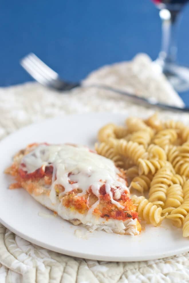 Fish Parmesan with rotini  pasta on a white plate.