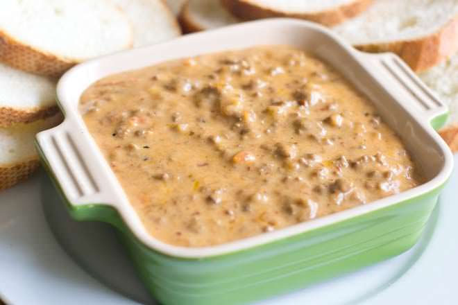 Cheesy hamburger dip in a square dish next to slices of bread.