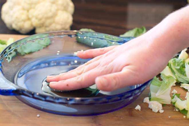 Rubbing oil around a blue glass pie plate.