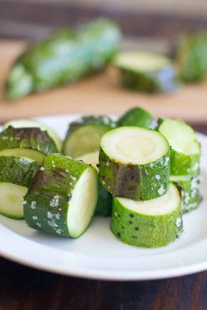 Slices of cooked zucchini with coarse salt on a white plate.