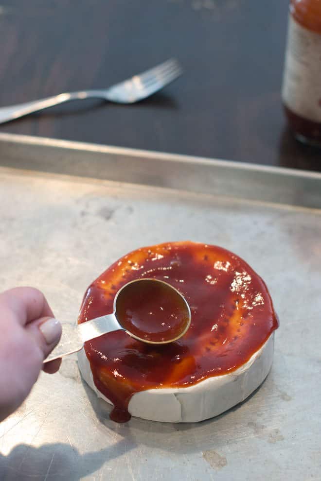 BBQ sauce being spread all over Brie with a measuring spoon.