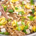 A wok with cooked farro, scrambled egg, green onion, and cashews