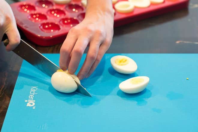 Cutting hard boiled eggs in half on blue board.