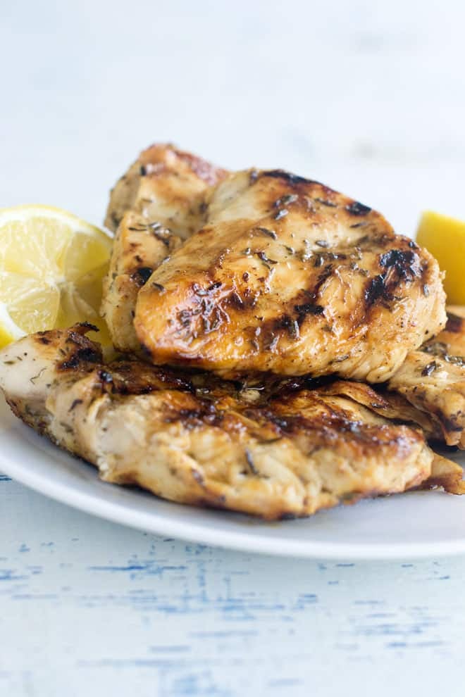 Grilled chicken breasts on white plate with lemon halves.