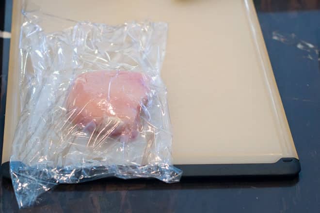 Raw chicken breast portion covered in plastic wrap.