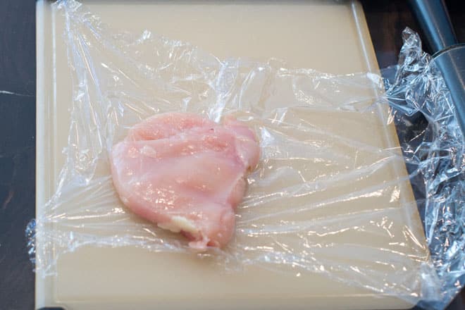 Chicken breast portion pounded to have the same thickness, on plastic wrap.