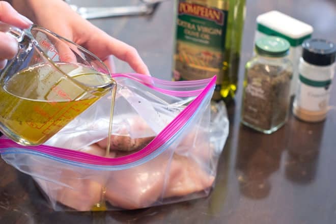 Marinade being poured into a ziptop bag with chicken inside, oil and spices in background.