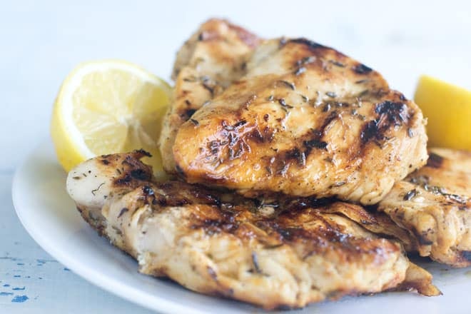 Grilled chicken breasts on a white plate with lemon.