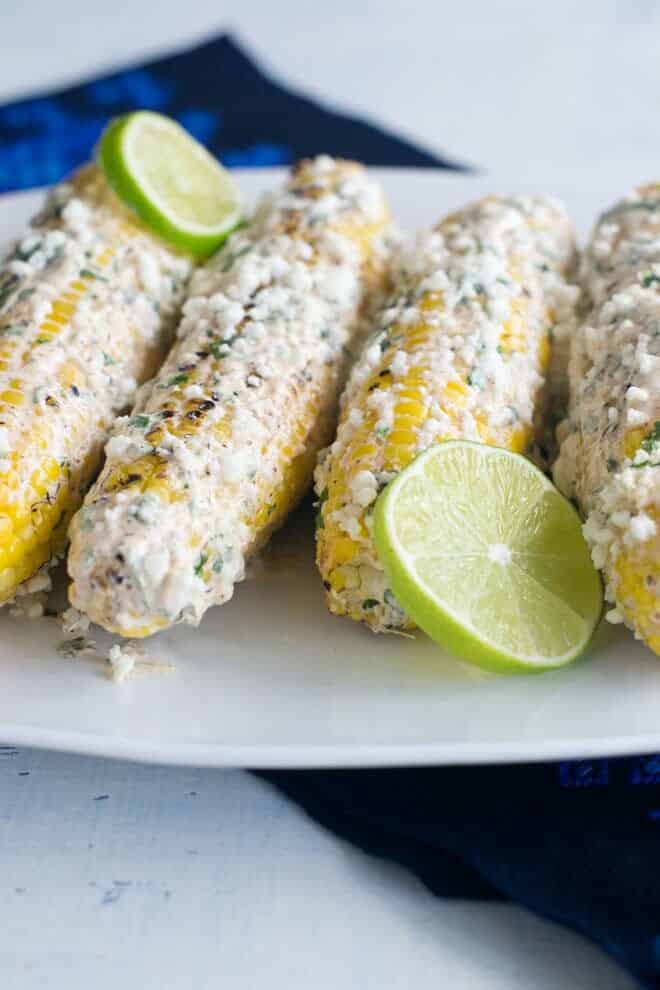 Elote corn on the cob on a plate with lime slices