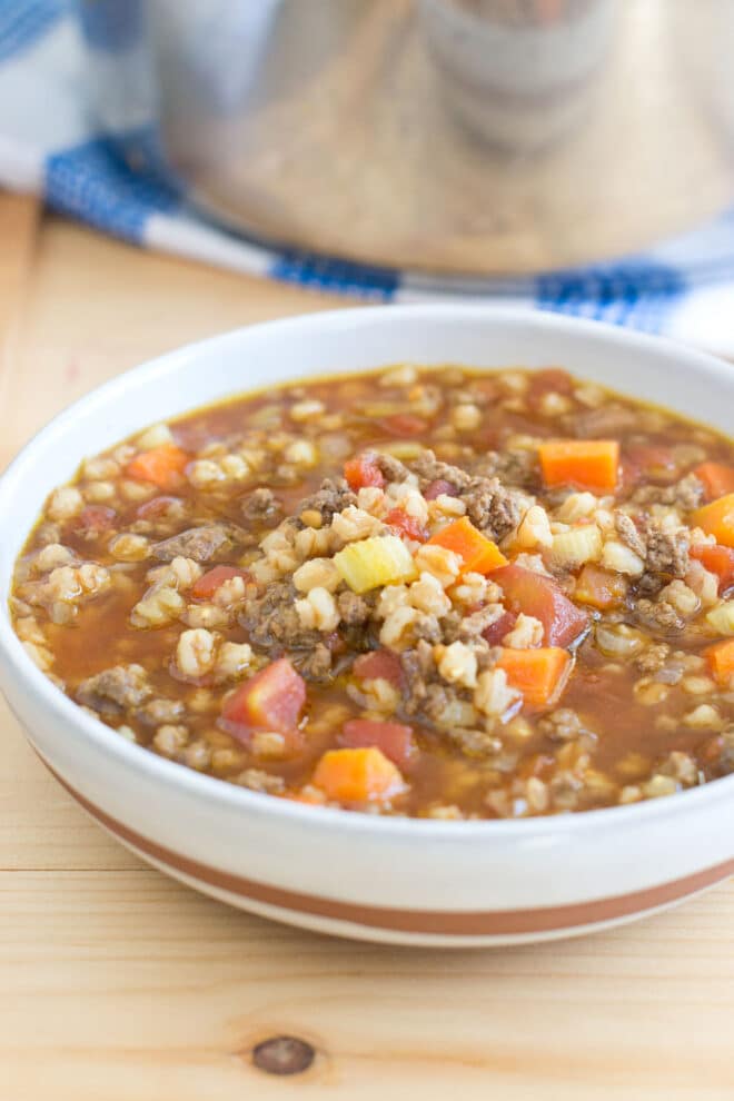 A bowl of beef and farro soup, the pot of soup in the background