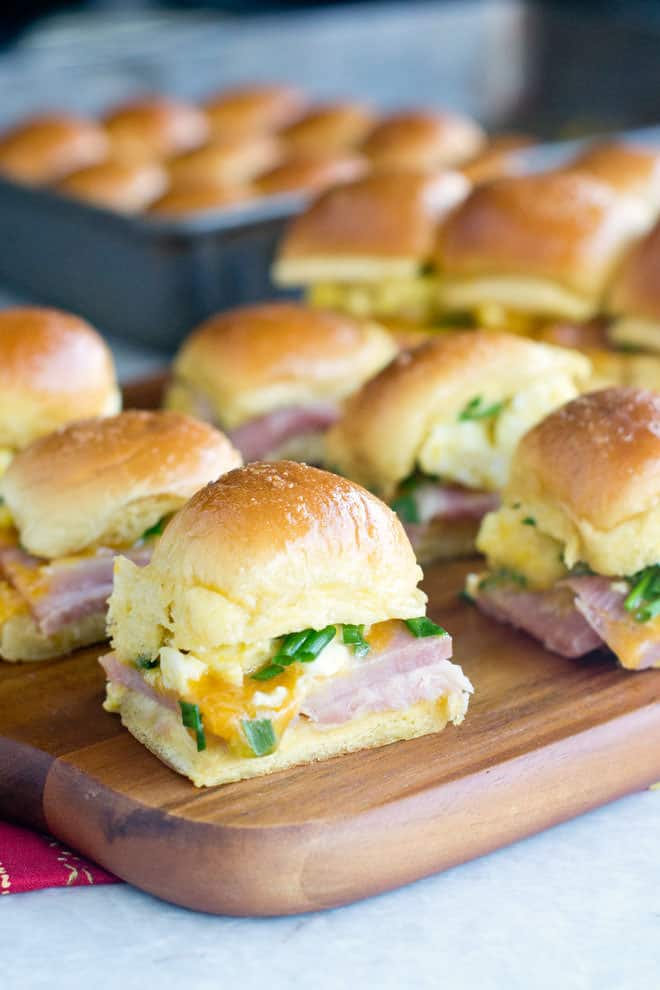 Lots of Breakfast sliders with eggs and ham on a wooden board.