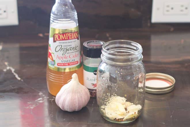 Garlic and spices at the bottom of a glass mason jar.