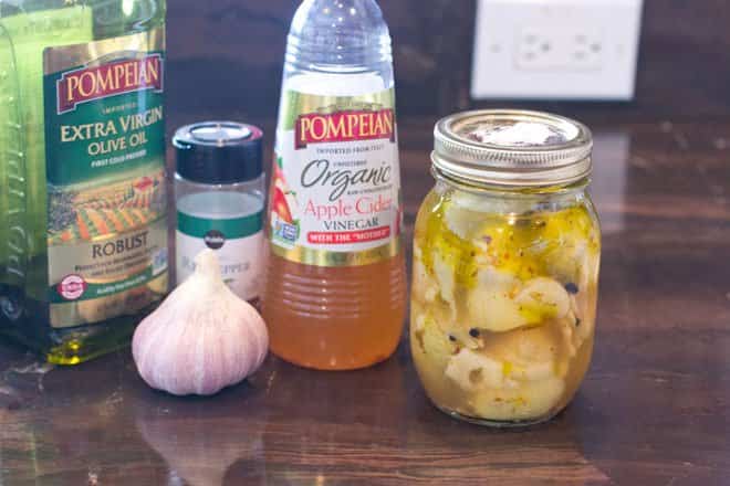 Mason jar of marinating artichoke hearts with ingredients around it.