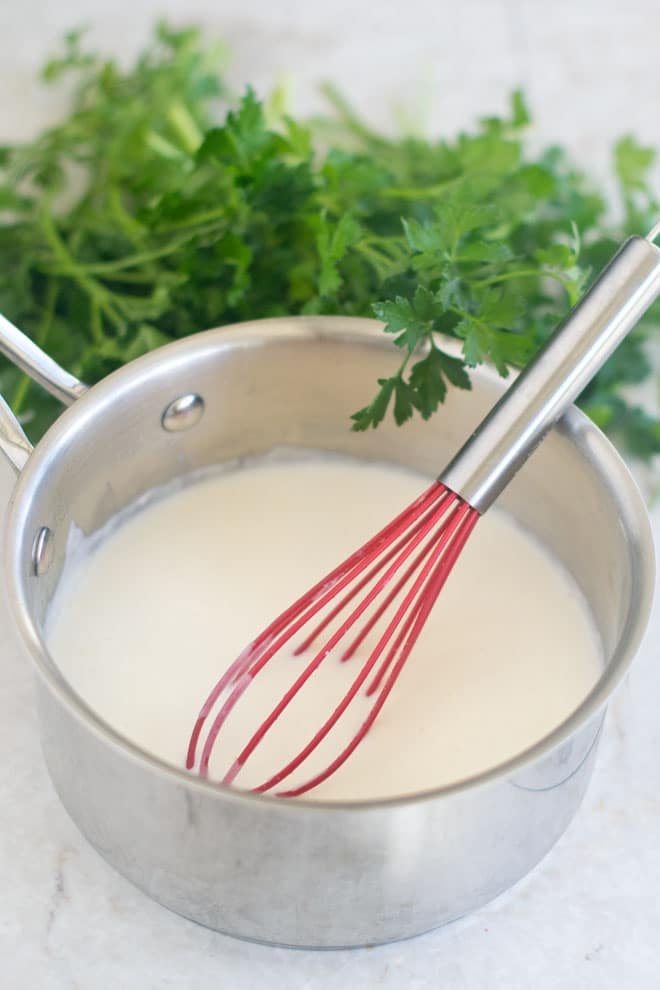 French béchamel sauce (white sauce) in a saucepan with a red whisk.