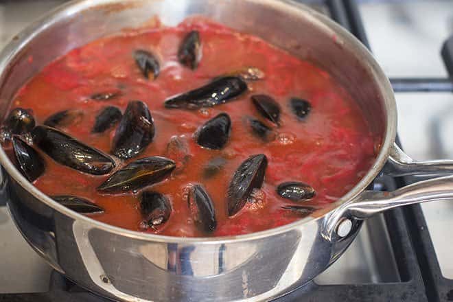 Mussels in tomato sauce on a pot on the stove.