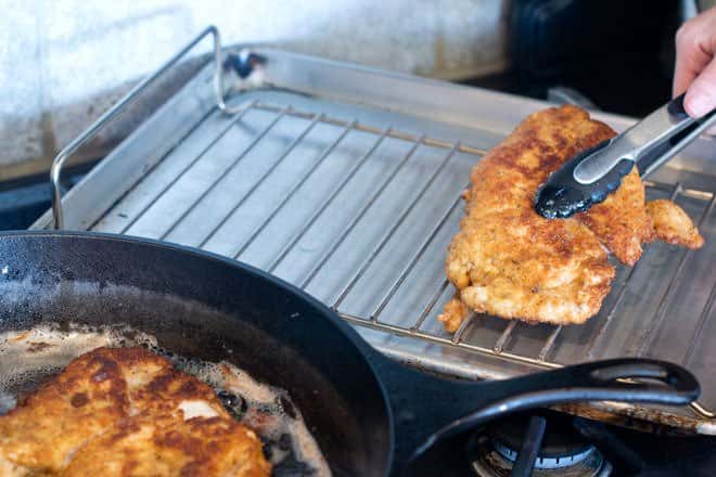 Using tongs to move chicken cutlets to rack on baking sheet.