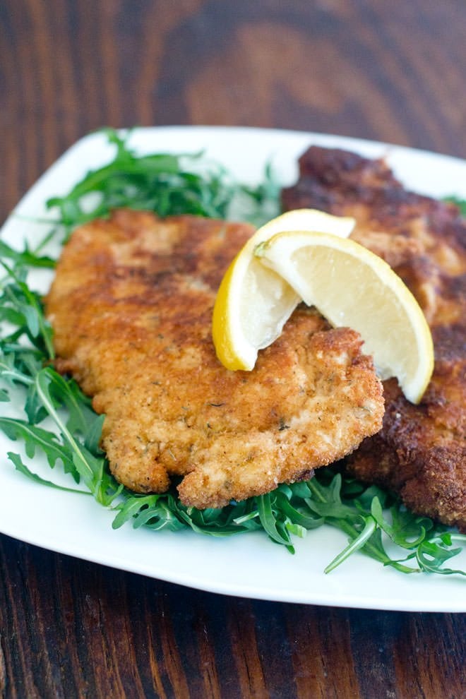 Breaded Chicken Cutlets on a plate with greens, topped with lemon wedges.