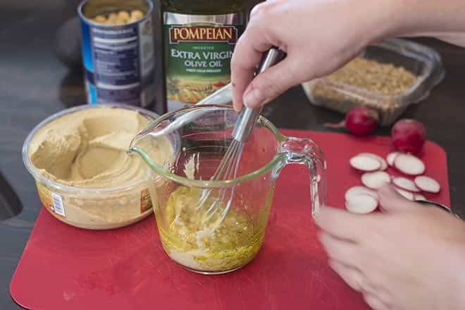 Hummus and olive oil being whisked together in a glass measuring cup.