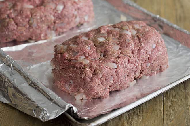 Ground meat shaped into a loaf for meatloaf, on a baking sheet lined with foil.