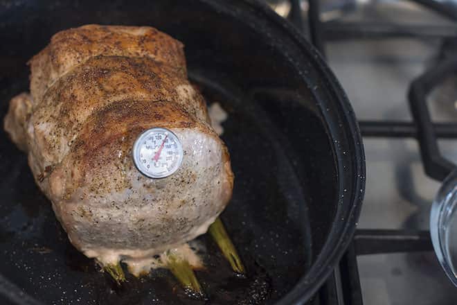 Cooked pork loin in roasting pan with instant read thermometer sticking out of the roast.