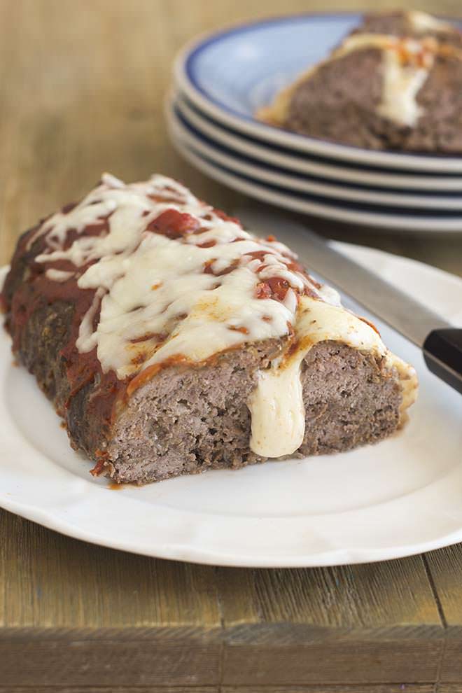 Meatloaf on a white plate with cheese oozing out of the middle.