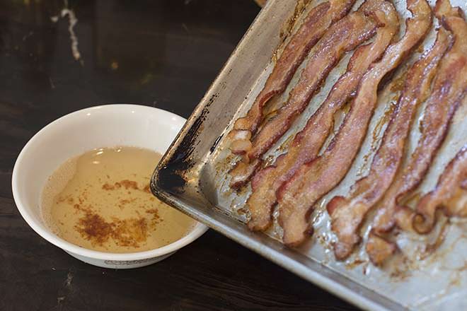 Baking sheet with bacon being tilted over a bowl to drain the fat.