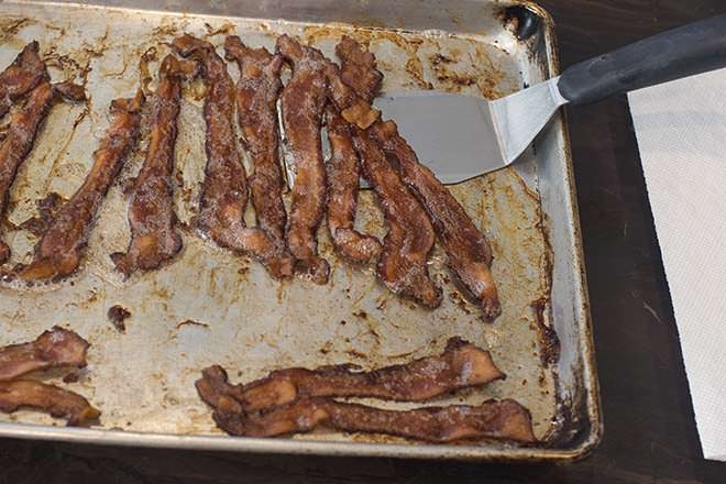 Cooked bacon being lifted off the pan with a metal spatula.