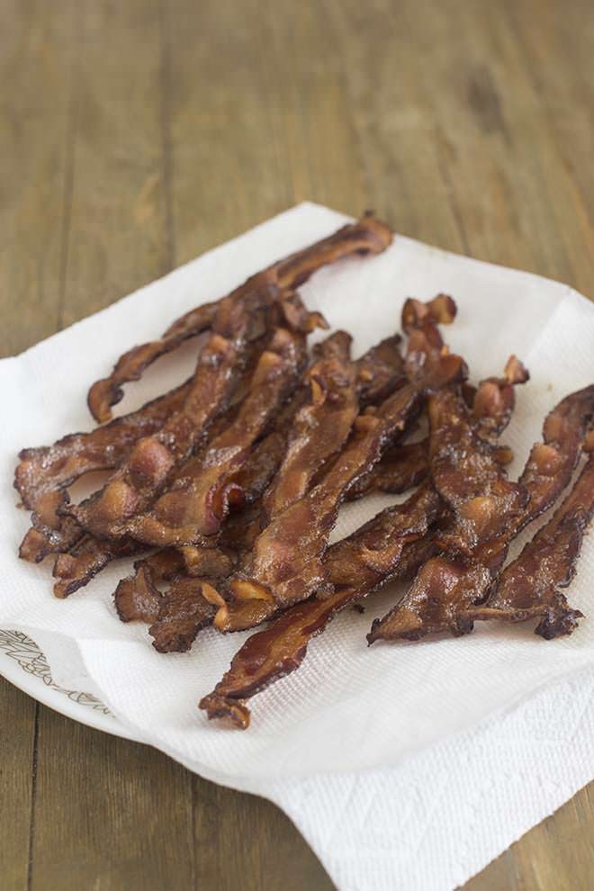 Pile of crispy bacon resting on a paper towel covered plate.