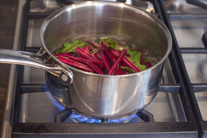 Beet greens and stems in pot with small amount of hot water.